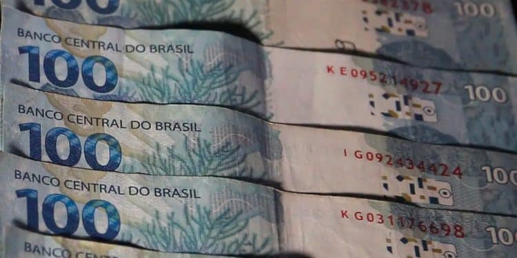 Notas de 100 reais enfileiradas, ilustrando os valores do abono salarial, do lote extra e do ressarcimento das cotas do PIS/PASEP.