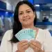 Mulher segura notas de R$ 100 em uma agência bancária, representando o saque de R$ 6.220 do FGTS.