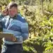 Profissional do setor agrícola analisando informações em tablet durante atividade em uma plantação.