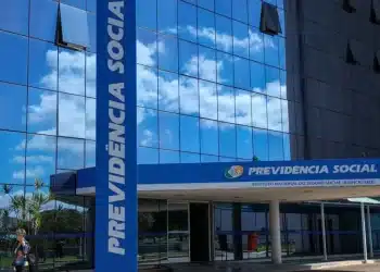 Fachada do edifício da Previdência Social (INSS) com reflexo do céu em vidro espelhado, simbolizando melhora no atendimento.