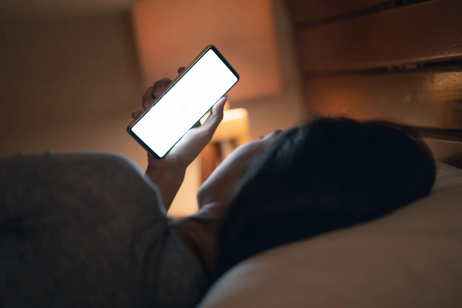 Pessoa usando o celular na cama durante a noite, representando as consequências do uso excessivo das redes sociais.