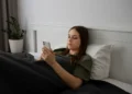 Jovem deitada na cama usando o celular, representando o uso excessivo das redes sociais e seus impactos no bem-estar.