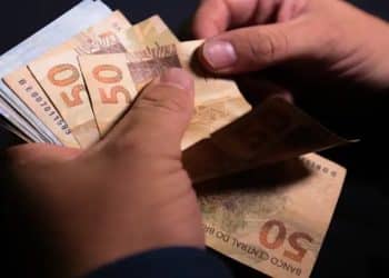 Mãos contam cédulas de cinquenta reais, representando o dinheiro esquecido que pode ser resgatado pelo Sistema de Valores a Receber