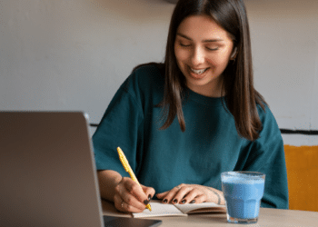 Jovem sorrindo estuda em casa com notebook.