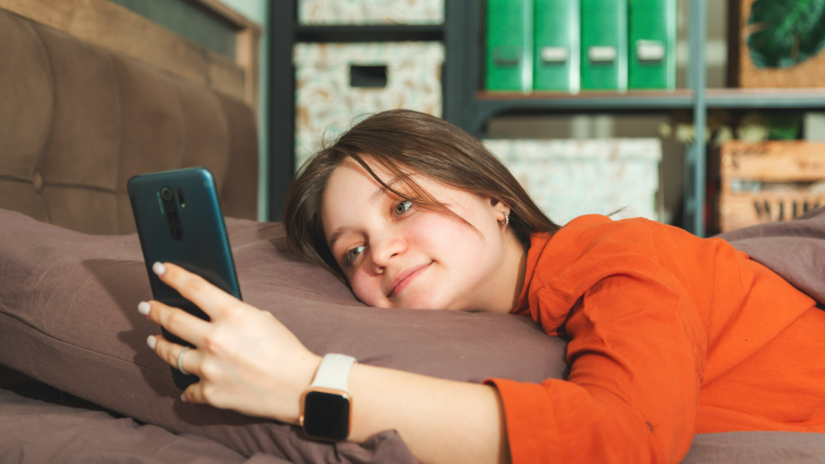 Jovem relaxa no sofá enquanto navega no celular em ambiente doméstico.