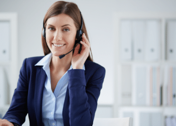 Atendente de call center sorrindo com headset em ambiente corporativo.