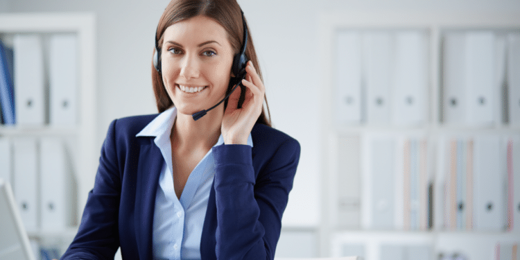 Atendente de call center sorrindo com headset em ambiente corporativo.