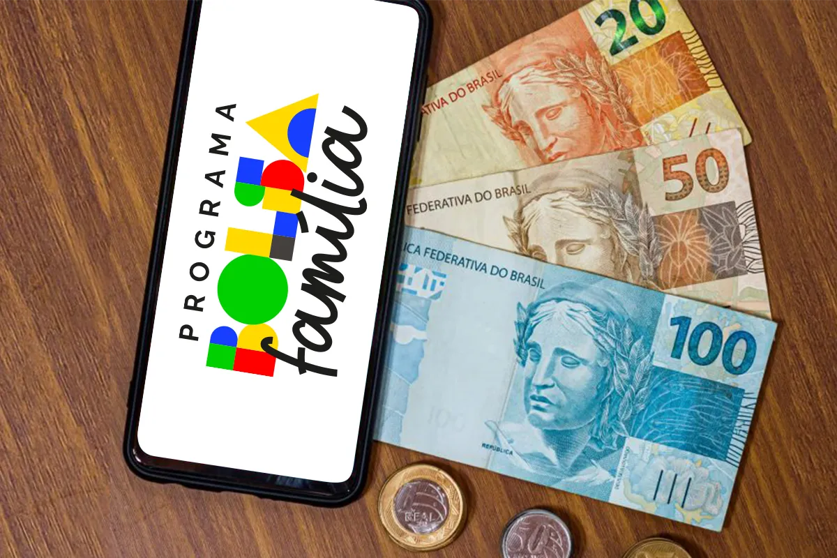 Celular com a identidade visual do Bolsa Família ao lado de cédulas e moedas de real.