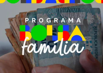Mãos seguram cédulas de real em imagem ilustrativa sobre o calendário do Bolsa Família de agosto.