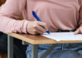 Estudante responde prova em carteira escolar de madeira.