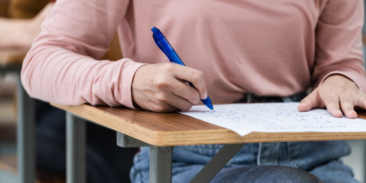 Estudante responde prova em carteira escolar de madeira.