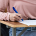Estudante responde prova em carteira escolar de madeira.
