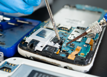 Técnico faz manutenção em placa de celular com ferramentas de precisão.