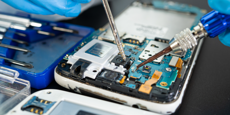 Técnico faz manutenção em placa de celular com ferramentas de precisão.