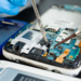 Técnico faz manutenção em placa de celular com ferramentas de precisão.