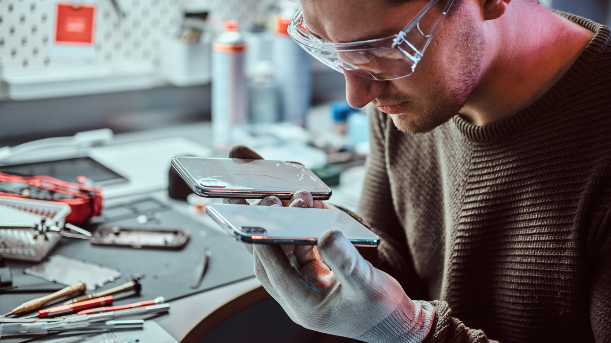 Técnico analisando celulares quebrados em bancada de manutenção.