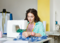 Jovem costureira trabalhando em ateliê moderno com máquina de costura.