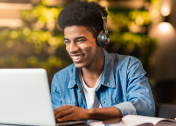 Jovem estuda online com fones de ouvido e notebook em ambiente aconchegante.