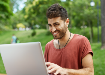Jovem usando notebook ao ar livre em ambiente de parque arborizado.