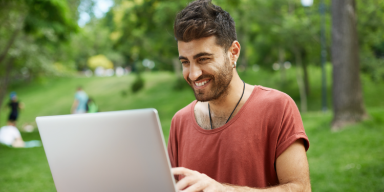 Jovem usando notebook ao ar livre em ambiente de parque arborizado.