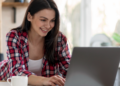 Jovem sorridente mexendo em notebook em casa.