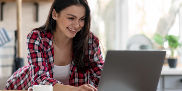 Jovem sorridente mexendo em notebook em casa.