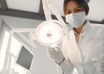 Dentista mulher realiza atendimento clínico sob luz branca no consultório.