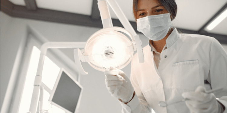 Dentista mulher realiza atendimento clínico sob luz branca no consultório.