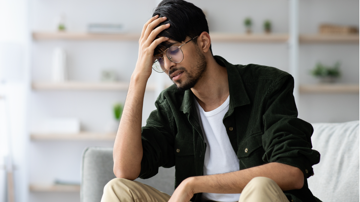 Jovem com expressão de preocupação sentado em ambiente doméstico.