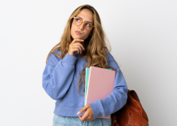 Estudante pensativa segurando cadernos com mochila marrom.