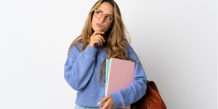 Estudante pensativa segurando cadernos com mochila marrom.