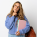 Estudante pensativa segurando cadernos com mochila marrom.
