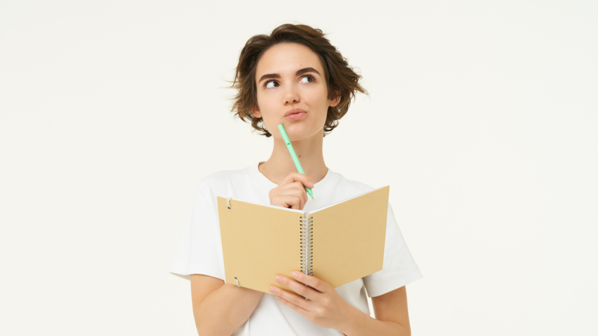 Jovem pensativa segurando caderno e caneta em fundo claro.