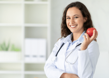 Nutricionista sorridente em consultório segura maçã vermelha.