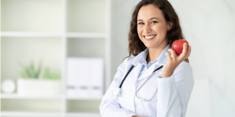 Nutricionista sorridente em consultório segura maçã vermelha.