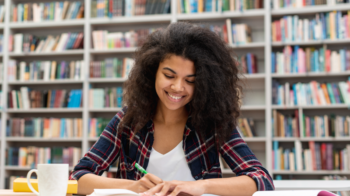 Jovem estudando concentrada em biblioteca moderna.