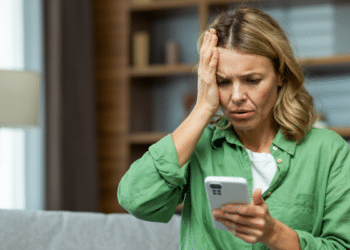 Mulher preocupada reage a mensagem no celular em casa.