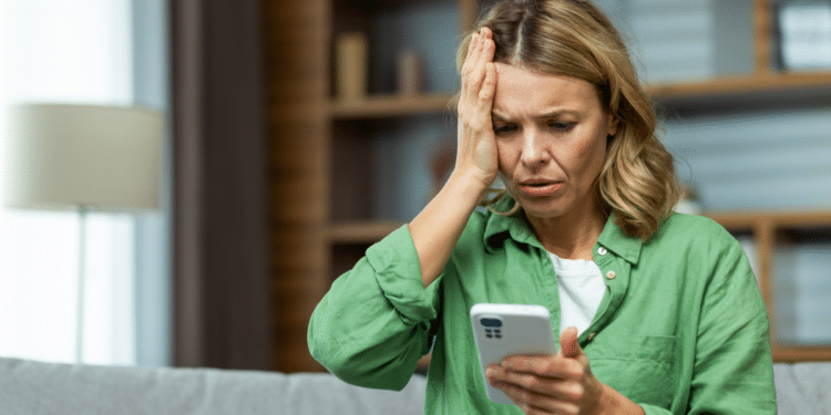 Mulher preocupada reage a mensagem no celular em casa.