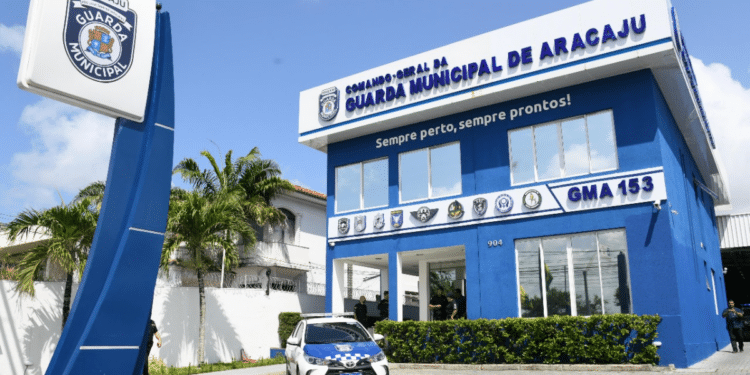Fachada azul da Guarda Municipal de Aracaju com placa, viatura oficial e agentes na entrada e entorno.
