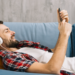 Homem ouvindo música relaxado no sofá com fone e celular.