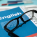 Materiais de estudo de inglês organizados em mesa com óculos.
