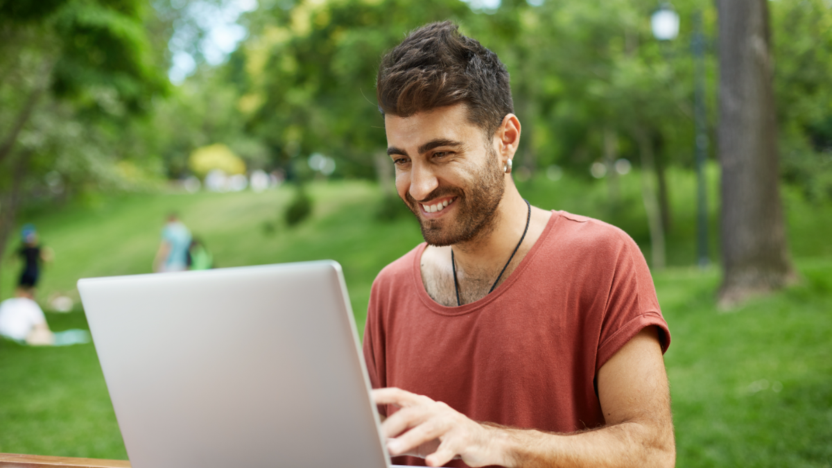 Jovem usando notebook ao ar livre em ambiente de parque arborizado.