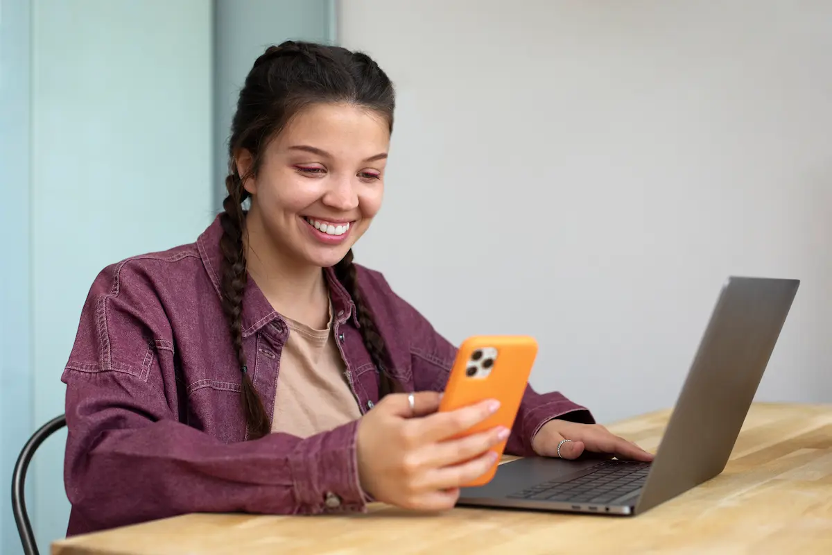 Jovem usa celular e notebook para realizar inscrição em programa de estágio.