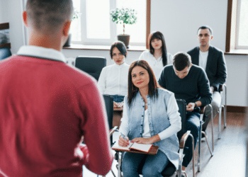 Pessoas assistem aula presencial com atenção em sala iluminada.