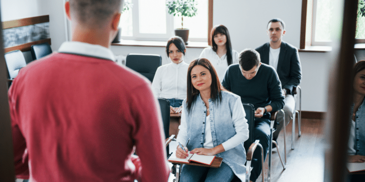 Pessoas assistem aula presencial com atenção em sala iluminada.