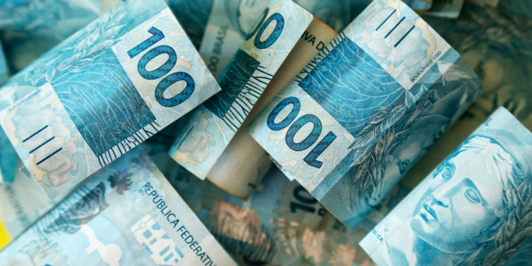 Cédulas de 100 reais brasileiras enroladas lado a lado em tom azul vibrante.