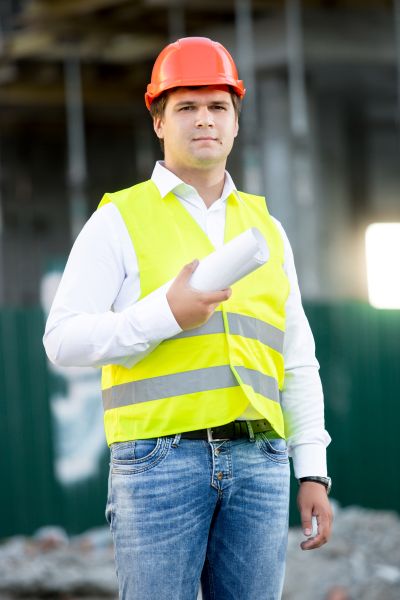 Mestre de obras com capacete laranja e projeto em mãos na construção.