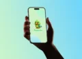 Mão segurando celular com tela do aplicativo Papuguinho para comunicação de crianças autistas.