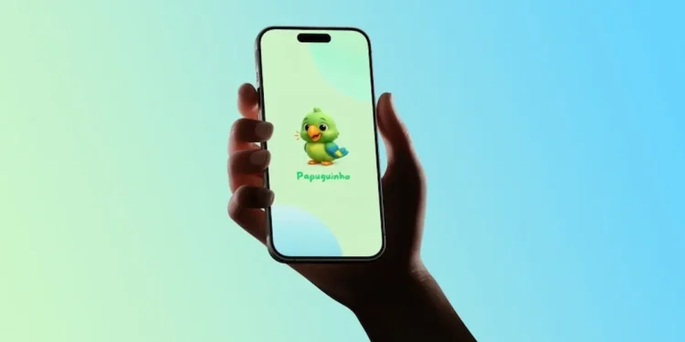 Mão segurando celular com tela do aplicativo Papuguinho para comunicação de crianças autistas.