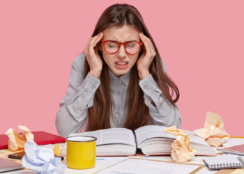Estudante estressada com dor de cabeça durante sessão de estudos.